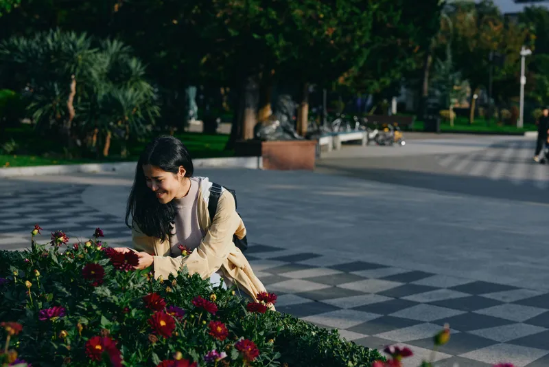 Woman admiring vibrant flowers in a park, outdoor garden scene with sunlight, candid moment of leisure, nature colors in an urban green space and peaceful atmosphere