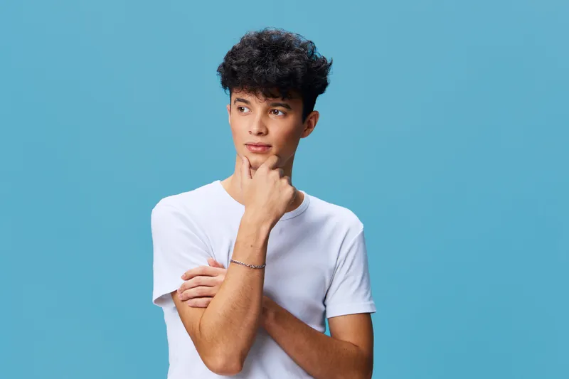 young man in white t-shirt thoughtfully looking away on blue background, casual style, curly hair, studio portrait, contemplative mood
