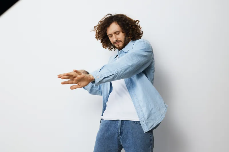 Young man in casual denim shirt and white t shirt stretching against a light background, conveying a relaxed and confident attitude, perfect for lifestyle and wellness themes