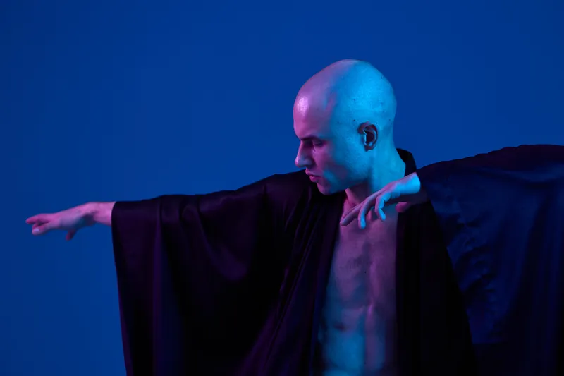 A striking image of a man exhibiting elegance in a flowing black robe, showcasing expressive movement against a vibrant blue backdrop. Ideal for fashion and artistry themes.