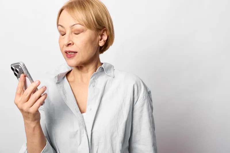 Woman with smartphone, senior older concern, technology texting communication, studio portrait with soft light on neutral background, close worried expression gaze