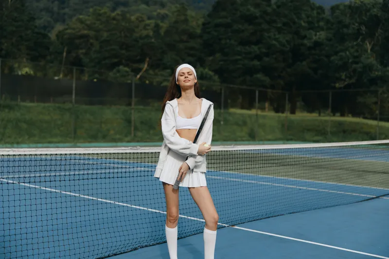 Young female tennis player in white sports attire on a tennis court, exuding confidence and joy in a vibrant green setting