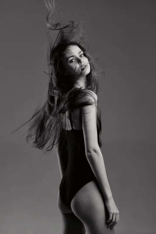 Black and white portrait of a young woman posing with flowing hair and confident expression in studio lighting.