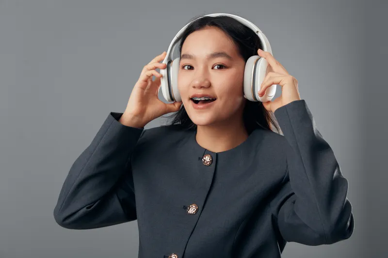 Young woman wearing headphones smiling and enjoying music with modern wireless technology. Portrait of cheerful girl in casual clothing listening to audio with hands touching headset.