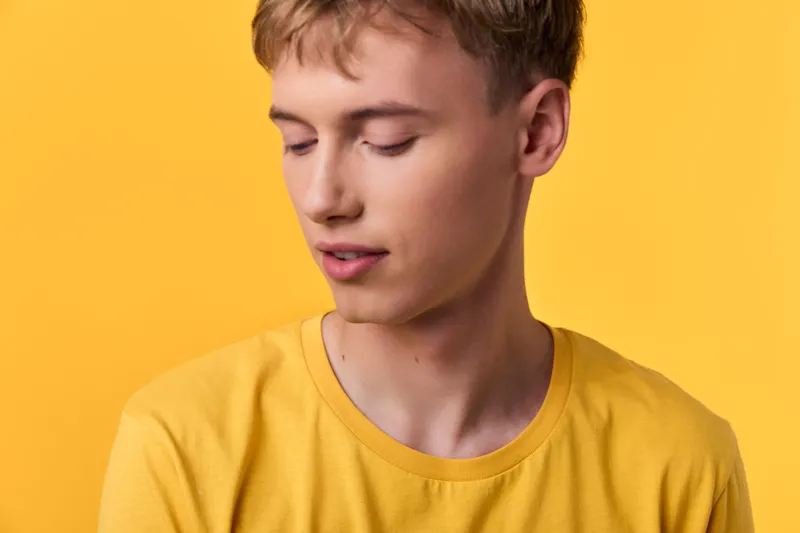 Young man wearing a bright yellow shirt stands against a matching yellow background, presenting a minimal, calm vibe with clean lines and studio lighting in a contemporary mood. Perfect for fashion,