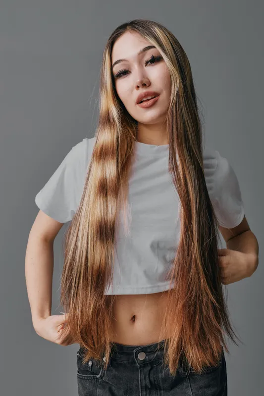 Young woman with long straight hair wearing white cropped t shirt and black jeans posing on gray background, beauty portrait and casual style with hands on hips and confident face.