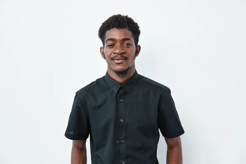 Young African man with dark skin wearing black short sleeve shirt standing and smiling on white background. Portrait of confident male with natural hair and casual style.