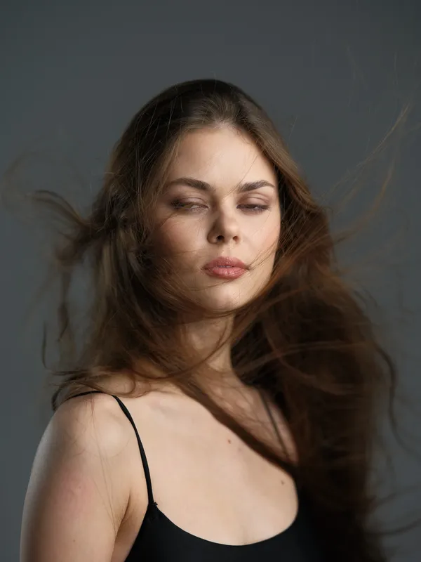 Portrait of a young woman with long brown hair flowing, wearing a black top, with a calm and serene expression.