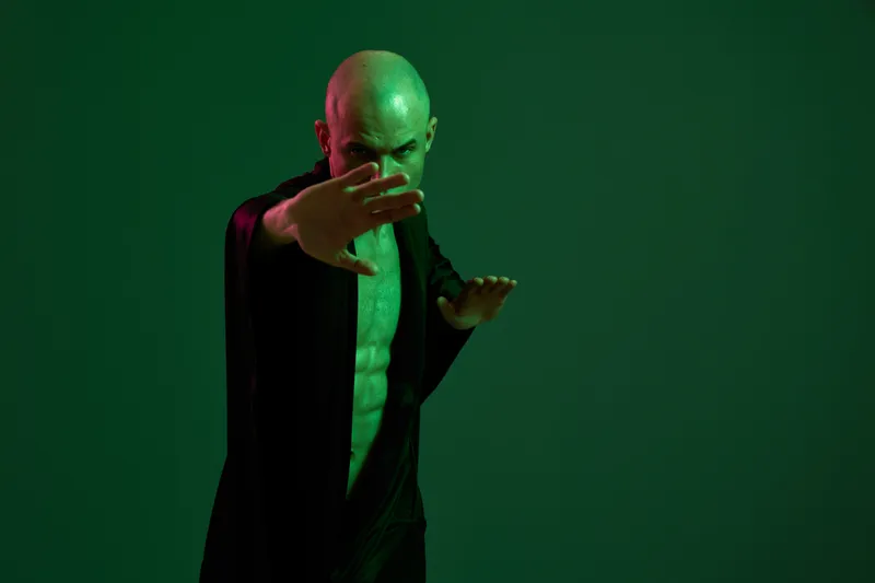 A focused man performs a martial arts stance, showcasing strength and intensity against a dark green background. His posture conveys determination and power.