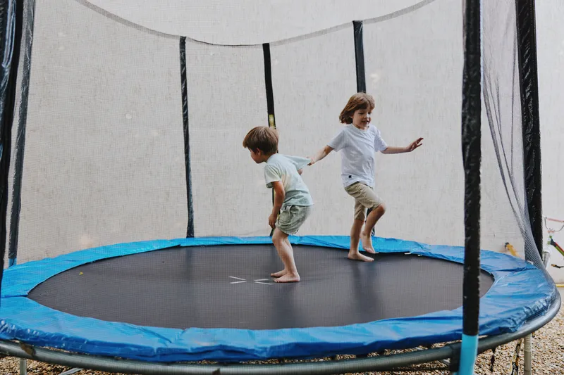 Two happy boys playing joyfully on a trampoline, showcasing their excitement and energy in a fun outdoor setting with a colorful background.