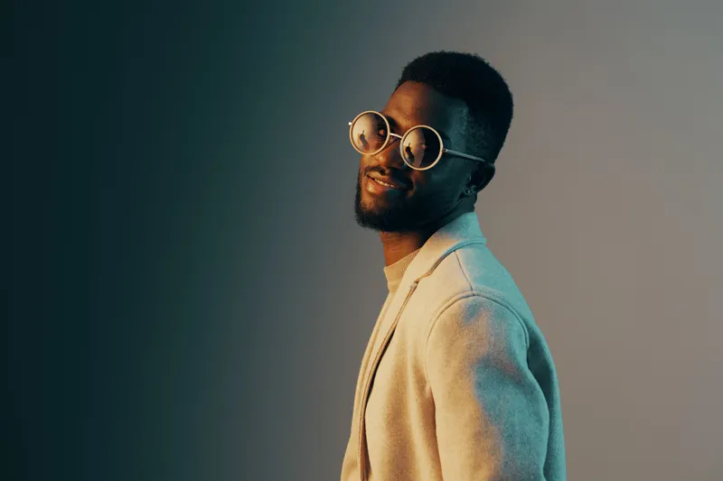 Stylish African man in fashionable sunglasses, smiling confidently against a gradient background with a modern aesthetic, portraying a youthful and trendy concept