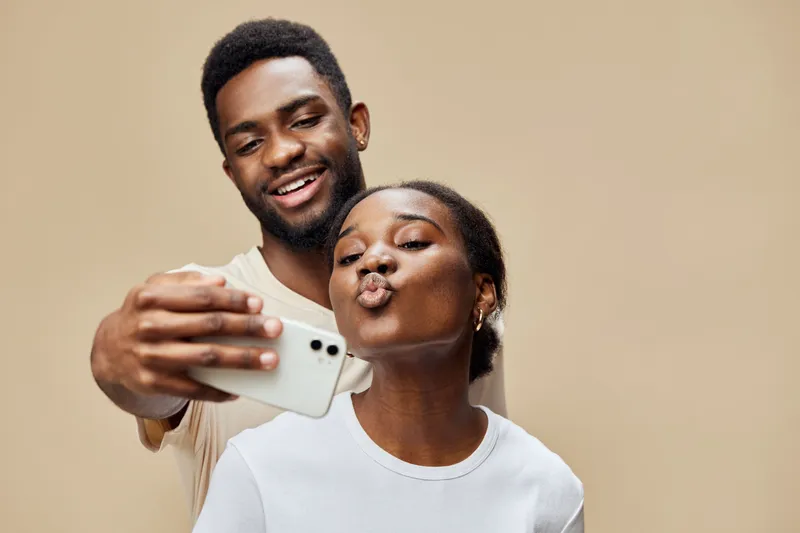 Cheerful young couple taking a selfie, demonstrating love and connection, with neutral background and bright clothing, perfect for social media themes