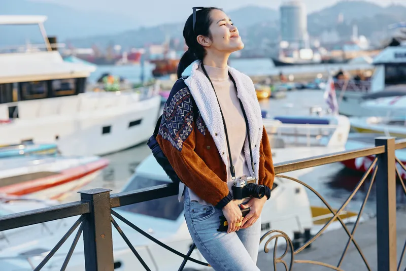 Fashion, streetwear and harbor scene with a stylish jacketed wearer posing by the quay, sunny day, casual denim, urban chic mood, travel inspired styling