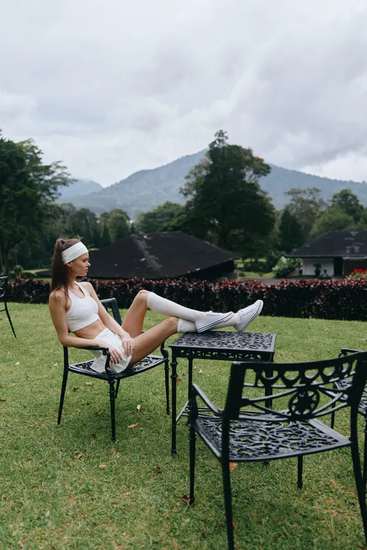 Young athletic woman relaxing outside in sporty clothes, showcasing wellness and tranquility amidst nature with mountains in the background