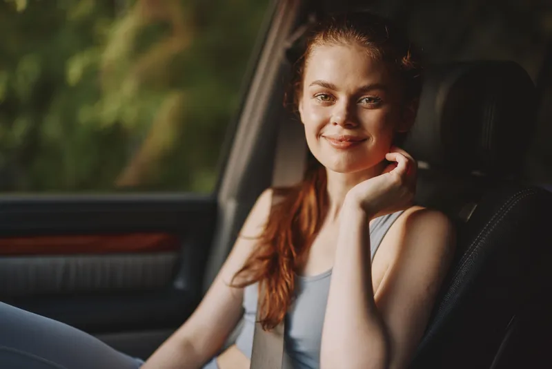 Young woman smiling in a car, wearing sporty attire, natural light background, healthy lifestyle concept