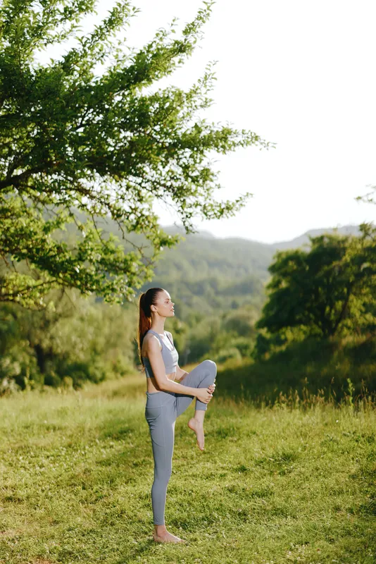 Young woman practicing yoga outdoors, showcasing flexibility and balance in a serene green setting, reflecting calmness and health