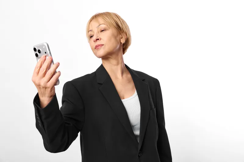 Woman smartphone black blazer studio white background portrait, holding mobile phone, communication and technology concept, modern lifestyle, soft light, neutral expression