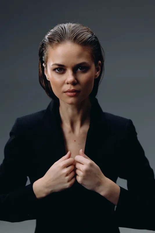 serious woman in black jacket with wet hair looking at camera, confident expression, dark background