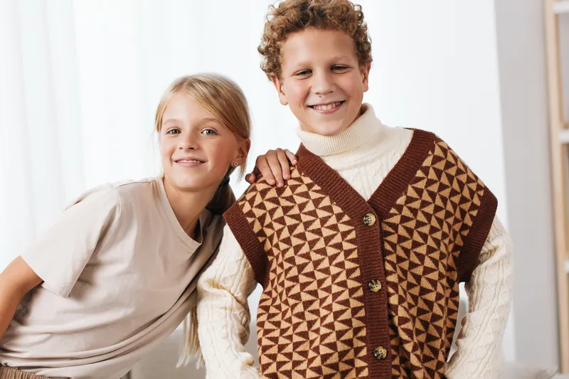 Authentic scene of play and school lifestyle, two cheerful children in knitwear share a moment at home, showcasing natural energy, friendship, and everyday joy.