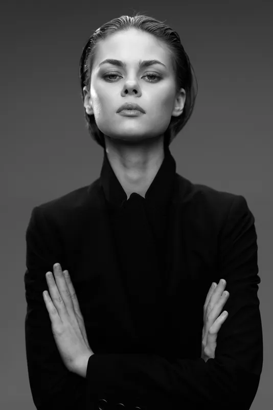 Confident woman in black jacket posing with crossed arms in black and white portrait with serious expression