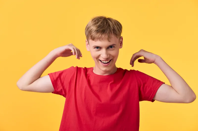 Smiling man red shirt flexing arms against yellow background, energetic confident mood shown in studio shot, bold colors and dynamic pose for lifestyle advertising