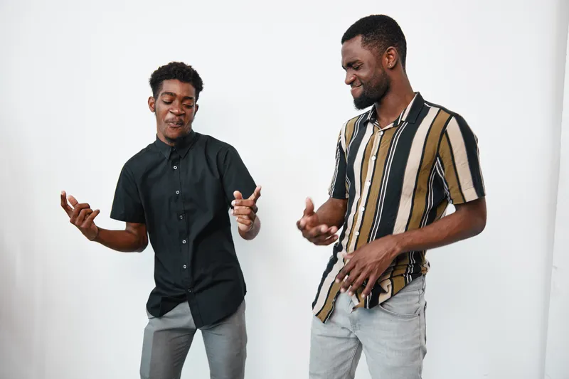 Two african american men dancing and enjoying music together in casual clothes with dark skin and joyful expressions on white background in studio setting.