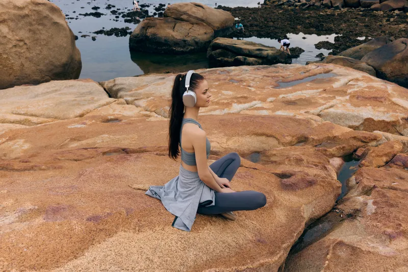 Young woman practicing meditation on rocky shore, wearing sportswear and headphones, showcasing tranquility amidst nature