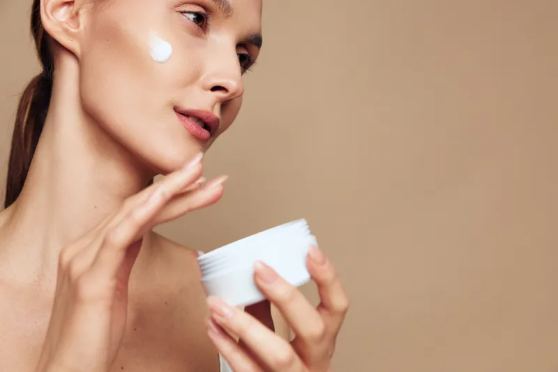 Portrait of a woman applying cream, close up on face, gentle skincare moment with soft lighting, natural tones, calm expression, subtle glow, everyday beauty