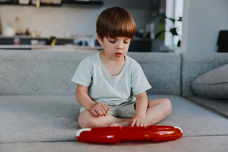 Concentrated boy playing with a toy, engaged in a moment of creativity while sitting on a comfortable sofa in a cozy living room environment.