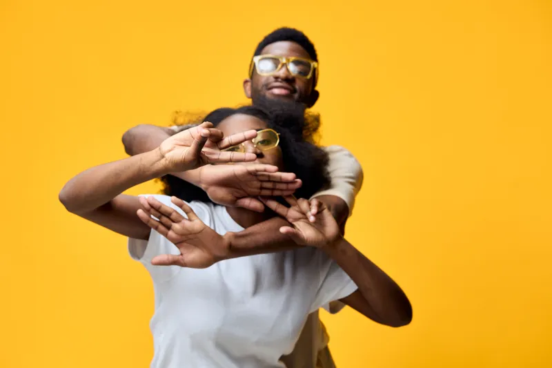 A joyful young couple poses playfully against a vibrant yellow background, showcasing modern fashion and a celebration of love and friendship