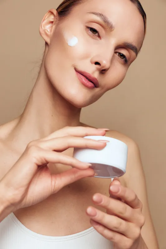 Woman skincare cream face beauty closeup, holds small jar, applying moisturizer on healthy skin, spa treatment mood, soft studio light, minimal background, fresh glow.
