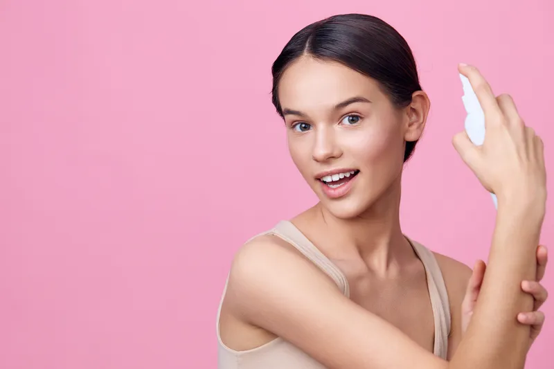 Young woman applying skincare product on her arm, showcasing healthy skin and confidence against a pink background, emphasizing beauty and self care