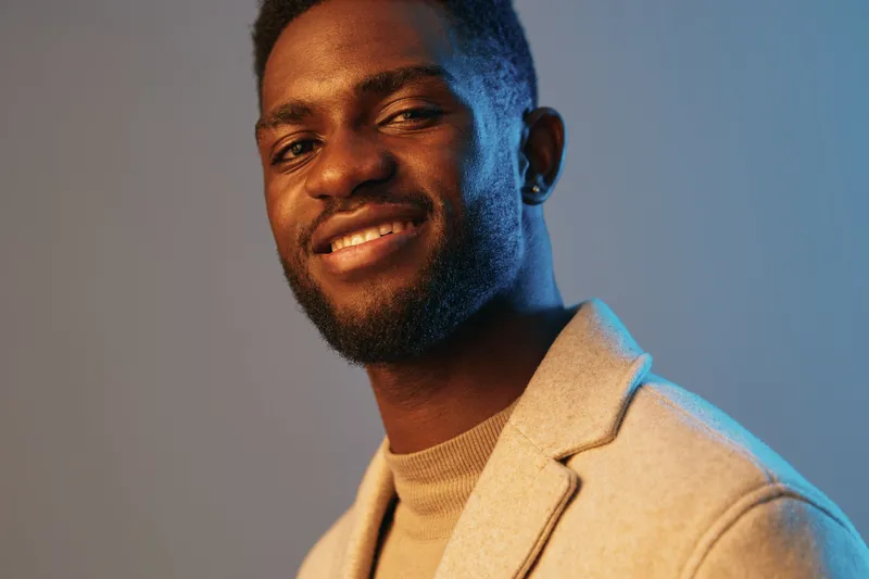 Stylish African American man smiling in a beige blazer against a blue gradient background, exuding confidence and modern elegance