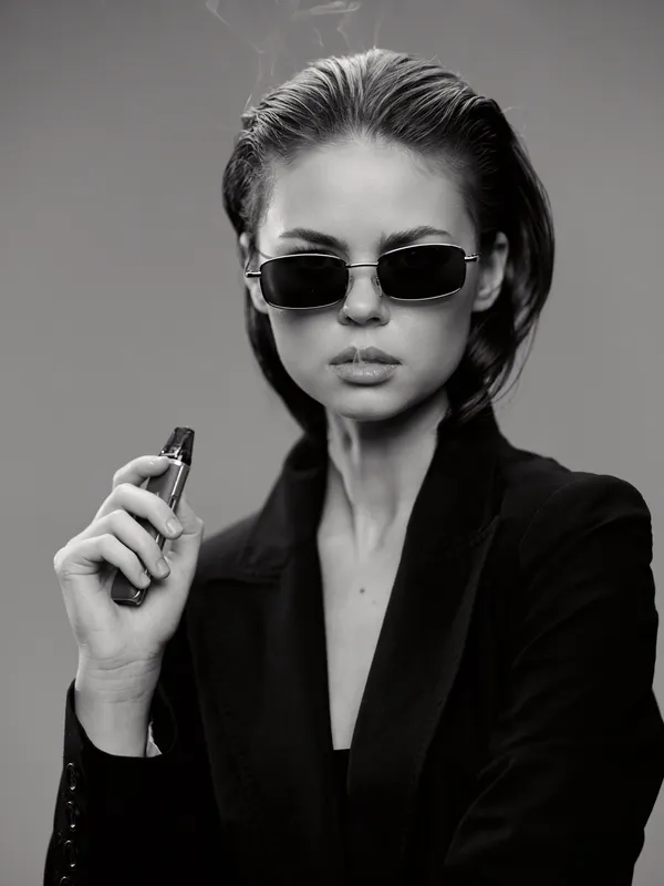 Stylish woman in sunglasses vaping with confidence in black and white portrait