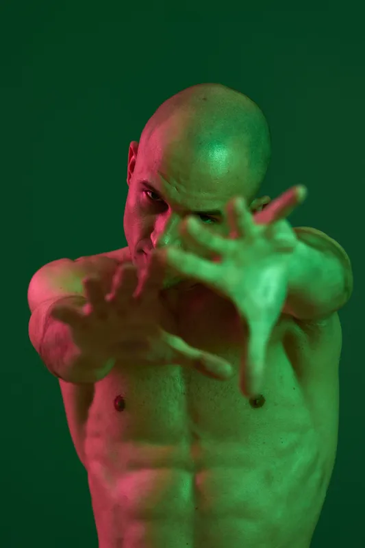 Athletic man showing dynamic pose with hands forward in vibrant green light, showcasing strength and confidence in contemporary style.