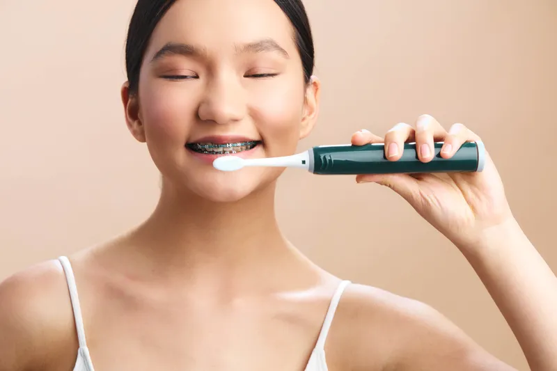 Asian woman smiles softly while brushing her teeth in a bright bathroom, capturing a daily hygiene moment that conveys freshness, health, and a confident, healthy lifestyle.