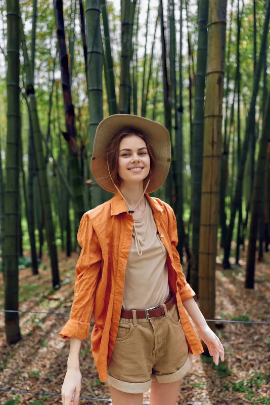 woman bamboo forest hat smile orange shorts nature portrait outdoors travel adventure young female smiling casual summer lifestyle among tall trees in a relaxed sunlit scene