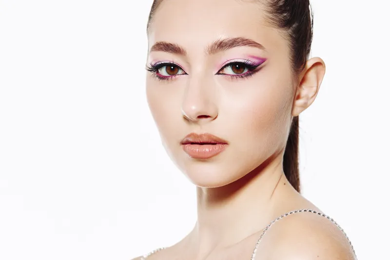 Closeup portrait of a young woman with trendy purple winged eyeliner and glossy nude lips. Studio shot on white background. Concept of beauty creativity and fashion makeup.