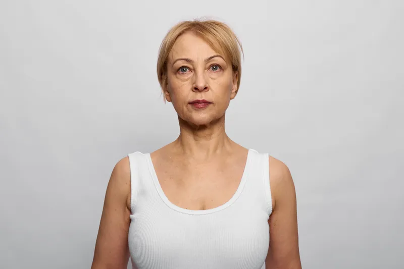 Woman portrait of mature senior lady, studio lighting, neutral background, looking at camera, calm facial expression, straight posture, minimalist composition, copy space