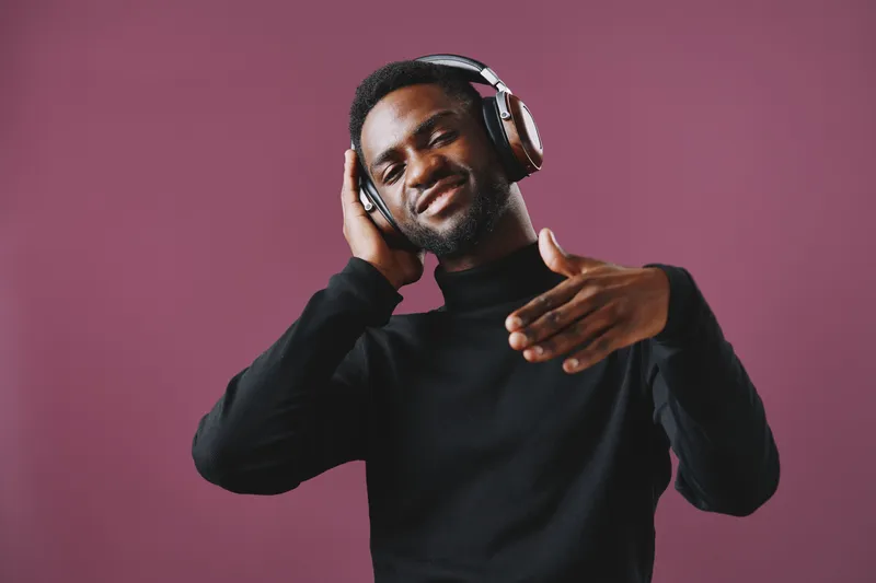 A stylish young man of African descent enjoys music with headphones, smiling confidently against a vibrant purple background Emotional and trendy vibe