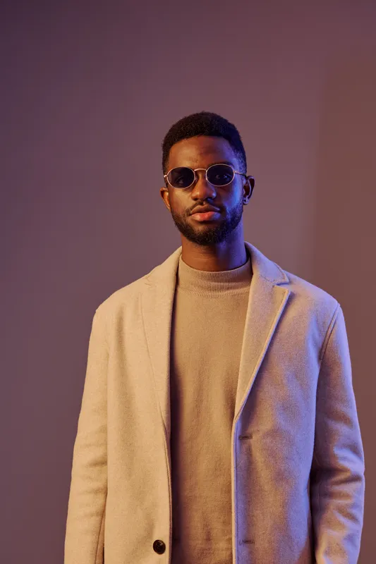 Stylish African American man in sunglasses poses confidently against a modern, colorful background, showcasing fashion and urban culture