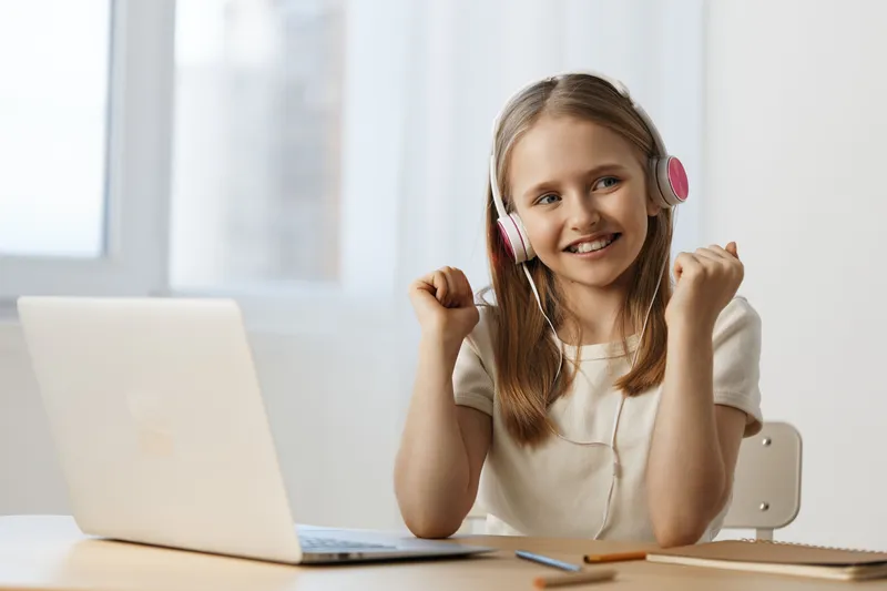Happy girl with headphones celebrating success at a laptop, enjoying online learning and cheerful atmosphere with bright colors and home office setting