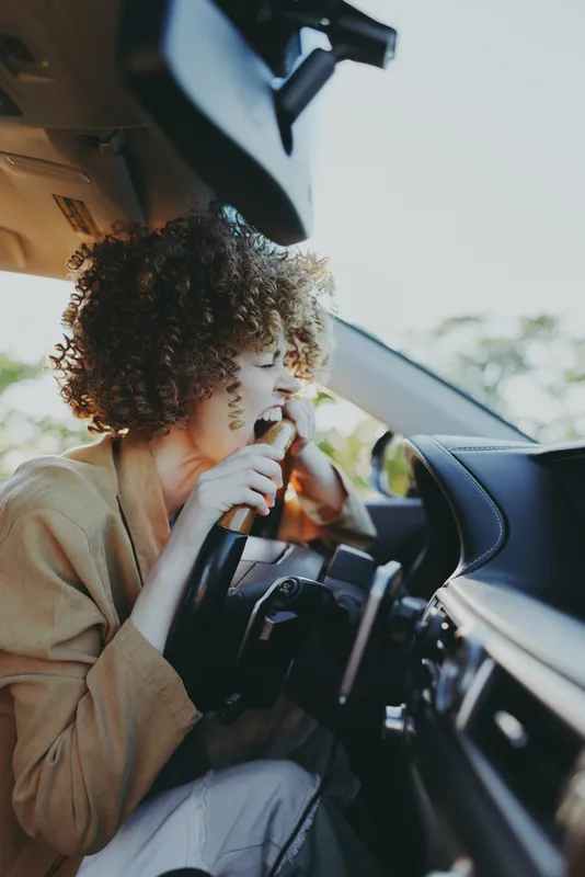 A driver woman with curly hair sings into a microphone inside a car, creating a candid road trip moment that blends a warm retro vibe with everyday autonomy and creative expression.
