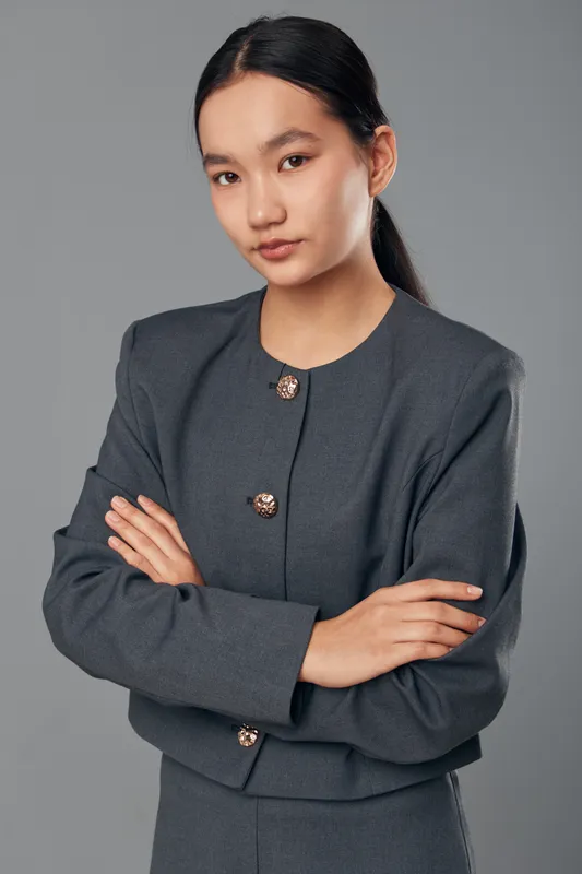 Young woman with crossed arms posing and looking at camera, wearing stylish gray business suit, professional confident model with neat hairstyle on neutral background.