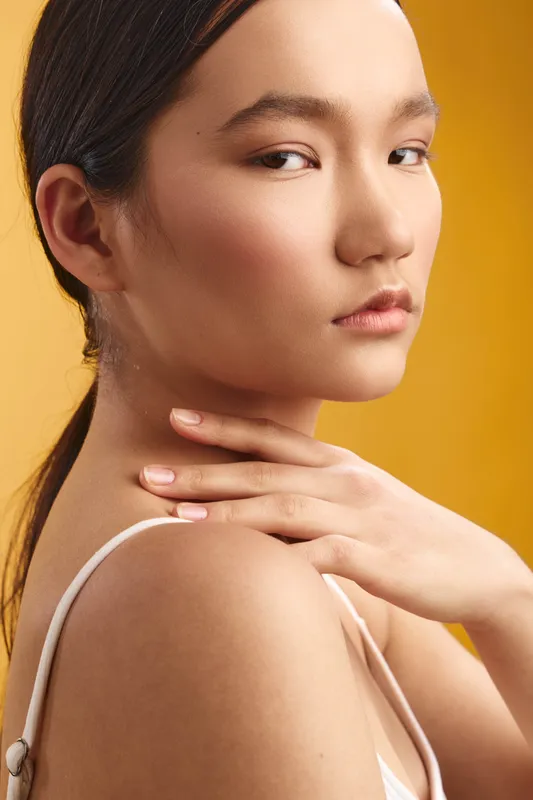 Asian woman exudes elegance as she poses in soft studio lighting, with a calm gaze and poised posture that convey grace, confidence, and refined beauty in a contemporary portrait.
