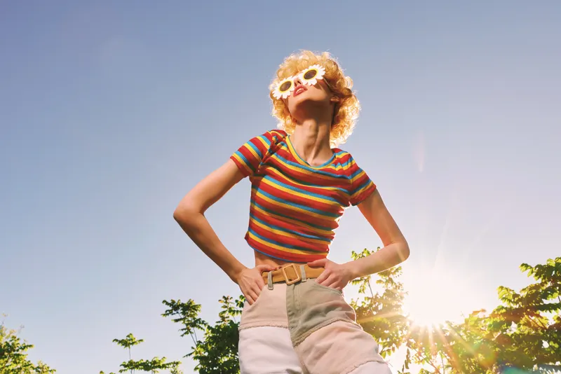 Smiling woman in a striped top and high waisted shorts outdoors, retro film color palette, sunlit scene capturing a carefree lifestyle and warm wellness vibe, in golden hour lighting
