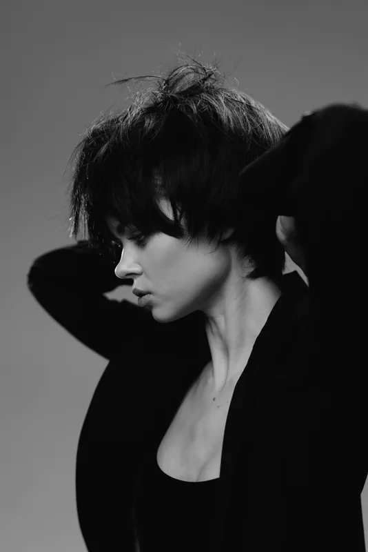 Black and white portrait of a young woman with short hair in a contemplative pose wearing dark clothing