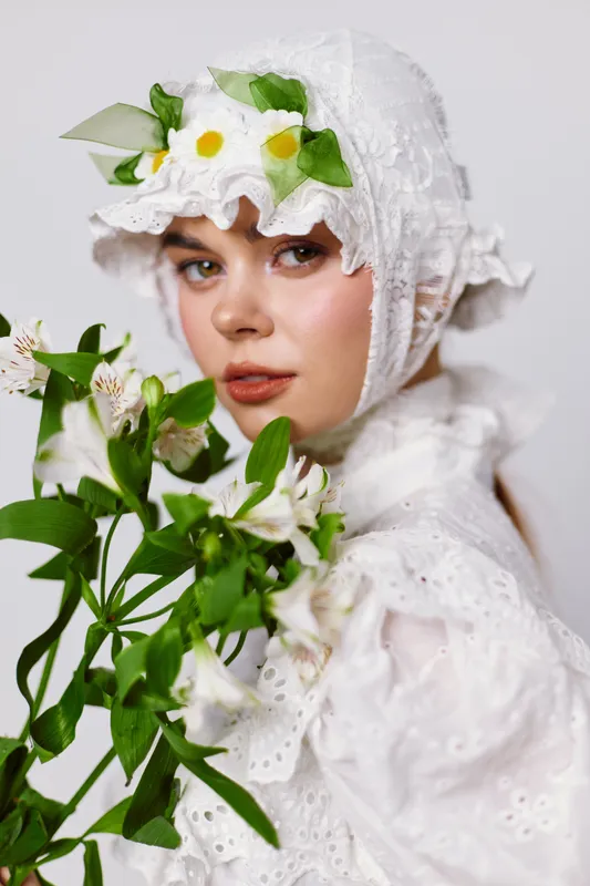Young woman in a floral white dress, holding white flowers, exuding serene emotions against a light background, representing themes of nature and purity