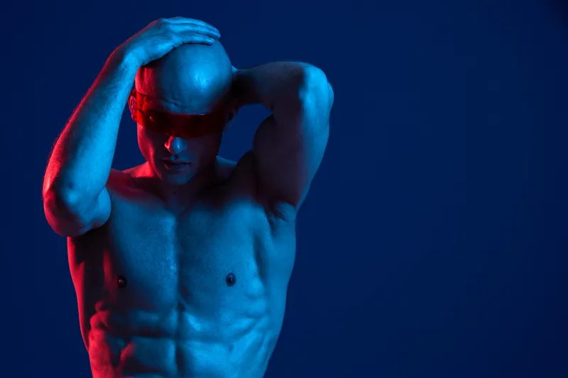 A striking image of a man in dramatic lighting with a blue tone, showcasing his chiseled physique and strong emotions, perfect for health and fitness-related themes.