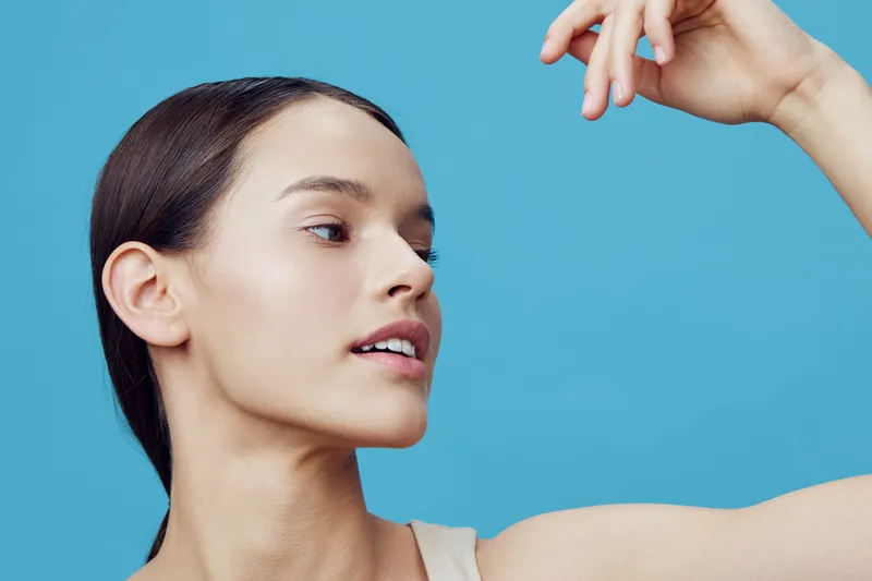 Portrait of a confident young woman with a natural look, showcasing healthy skin against a vibrant blue background Ideal for beauty and wellness concepts